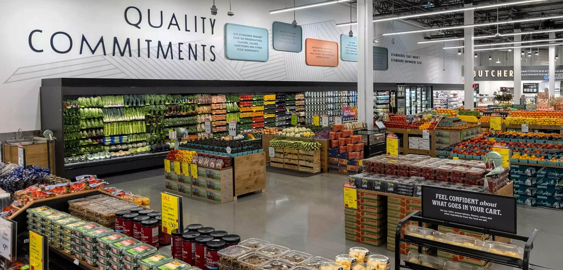 Whole Foods Market supermarket chain known for selling natural and organic food products. The store environment is designed to be inviting and educational for customers. The company emphasizes strict quality standards and a commitment to sustainable agriculture. The text in the image highlights the store's "Quality Commitments" and encourages customers to "feel confident about what goes in your cart".