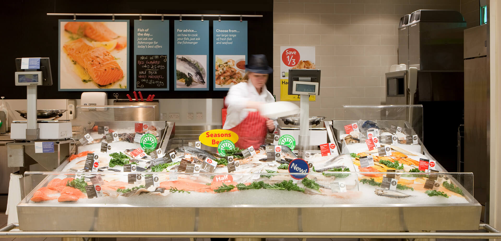 Hipermercado Tesco Extra, Accrington, Lancashire, Reino Unido. El mostrador de "Pescado del día" ofrece diversos tipos de pescado fresco, presentado en hielo, con letreros que dicen "Pregunte al pescadero si necesita consejos sobre cómo cocinarlo".
