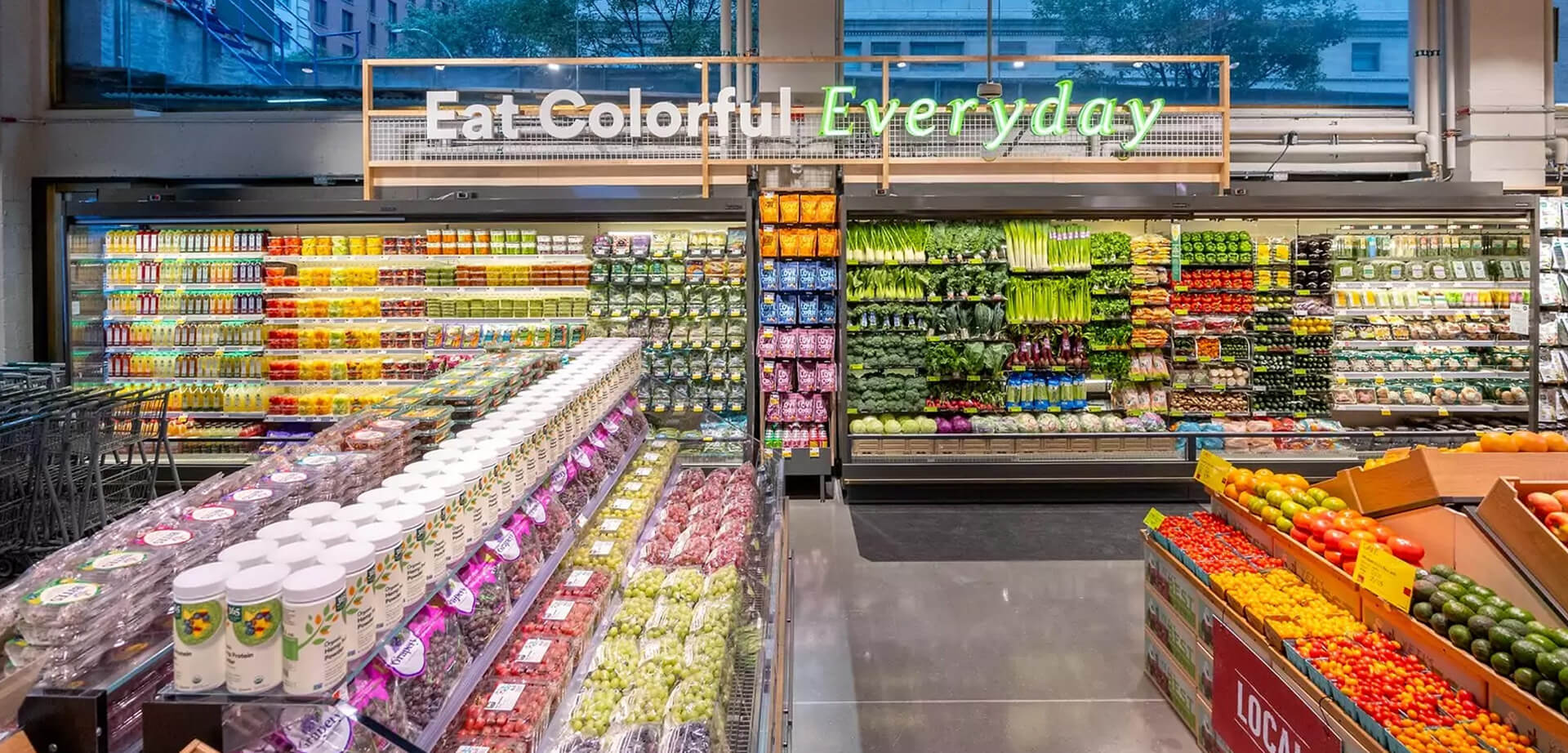 Tienda Whole Foods Market Daily Shop, con especial énfasis en la sección de productos frescos. El eslogan "Come colorido todos los días" es un elemento destacado del concepto de diseño de la tienda, que enfatiza la variedad y los beneficios para la salud de las frutas y verduras coloridas. Ubicada en el barrio de Lenox Hill de Manhattan, Nueva York.