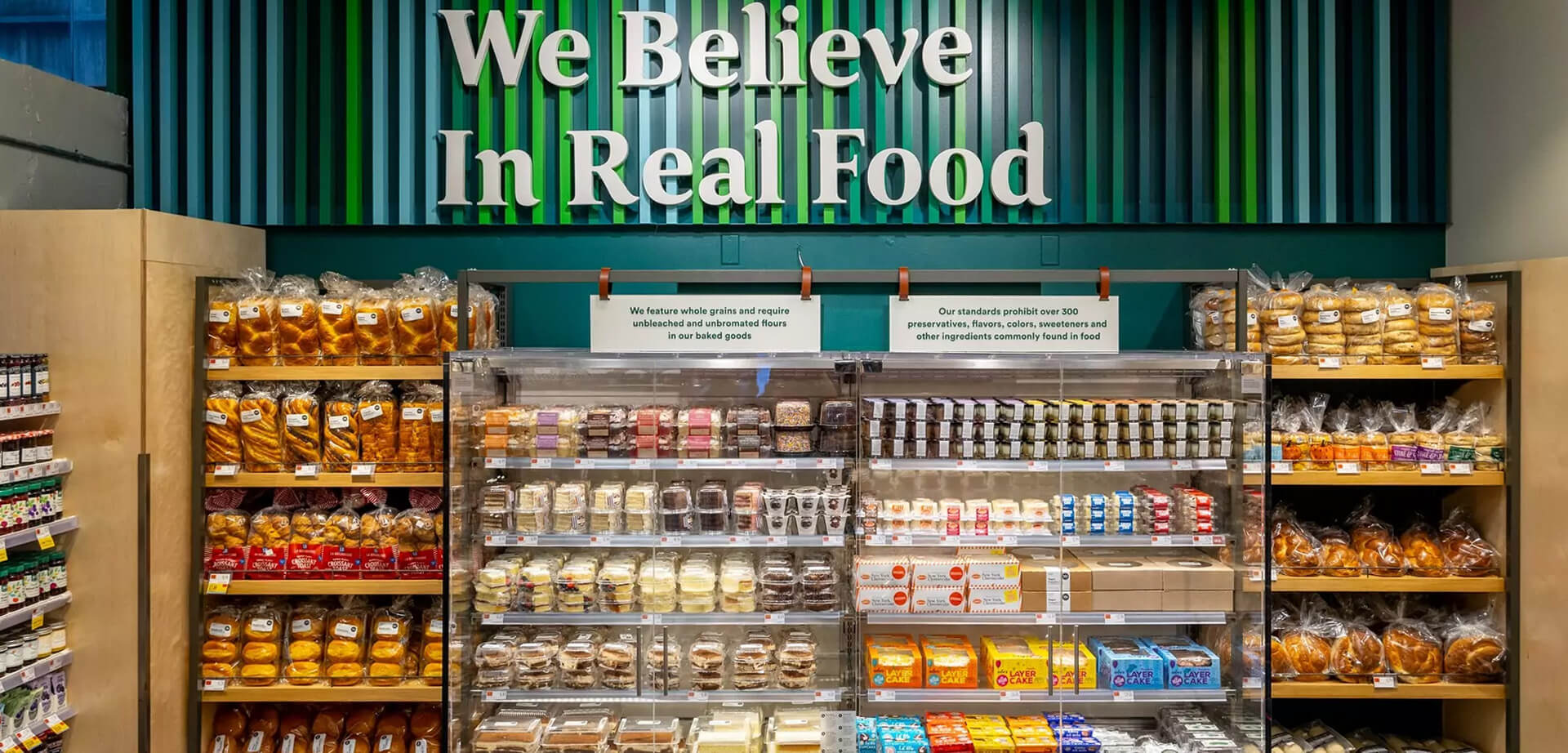 La sección de repostería de Whole Foods Market destaca la filosofía y los estándares de calidad de la tienda: "Creemos en la comida real". El texto enfatiza el uso de ingredientes específicos y la eliminación de aditivos artificiales comunes.