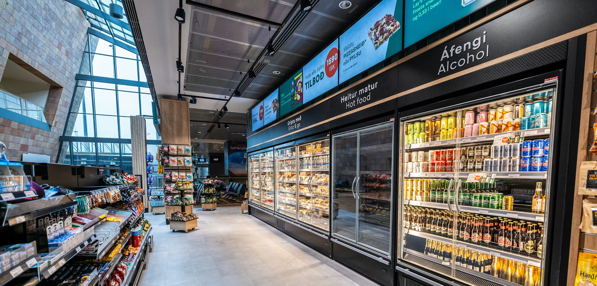 Dieses Bild zeigt offenbar das Innere eines Ladens am Flughafen Point KEF in Island. Dieser Convenience-Store bietet eine Vielzahl an Reiseartikeln, Snacks und Getränken, darunter sowohl „Heitur matur“ (warme Speisen) als auch „Áfengi“ (alkoholische Getränke), wie die isländische Beschilderung zeigt.