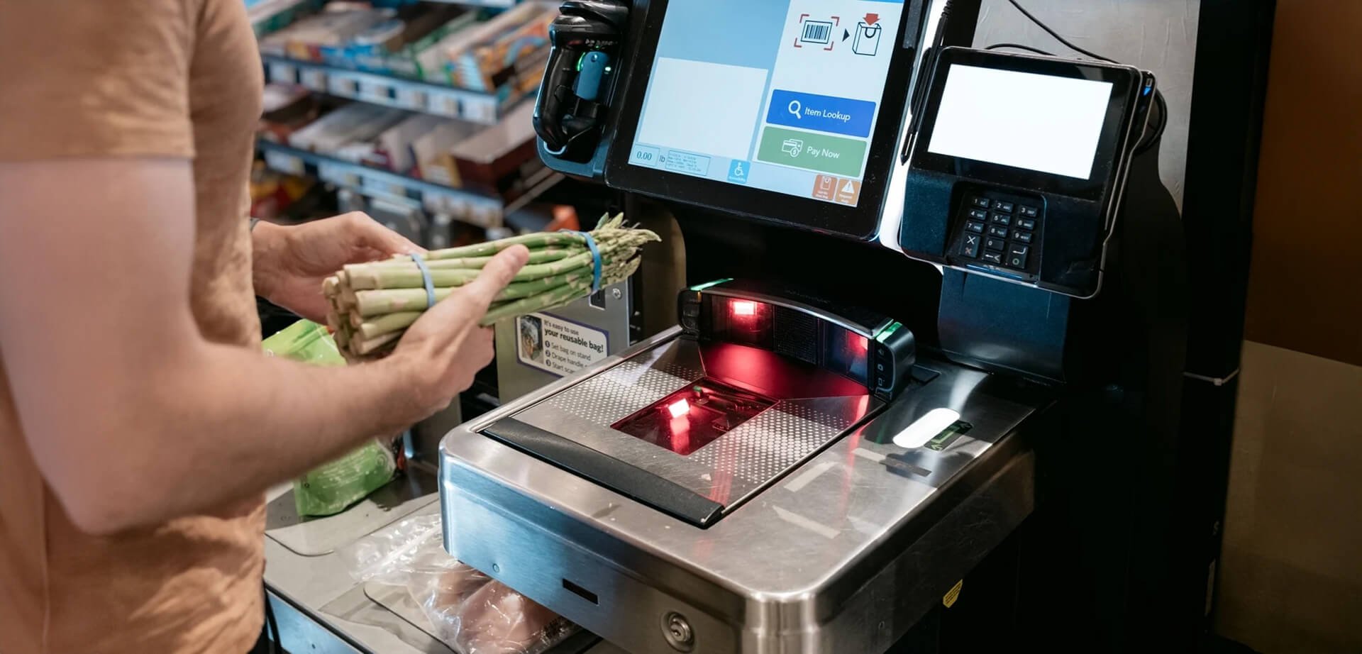 Das Bild zeigt eine Person an einer Selbstbedienungskasse in einem Supermarkt. Diese Technologie ermöglicht es Kunden, ihre Einkäufe selbstständig zu scannen, einzupacken und zu bezahlen, ohne dass ein Kassierer benötigt wird.