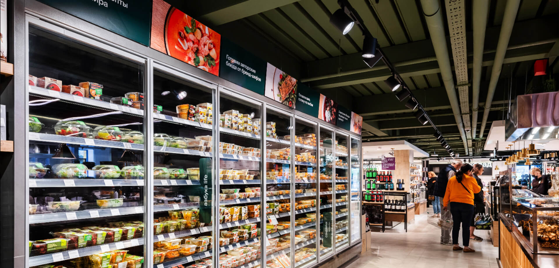 Azbuka Vkusa Supermarkt-Gang mit einer großen Auswahl an abgepackten Gerichten und frischen Produkten in Kühlvitrinen.