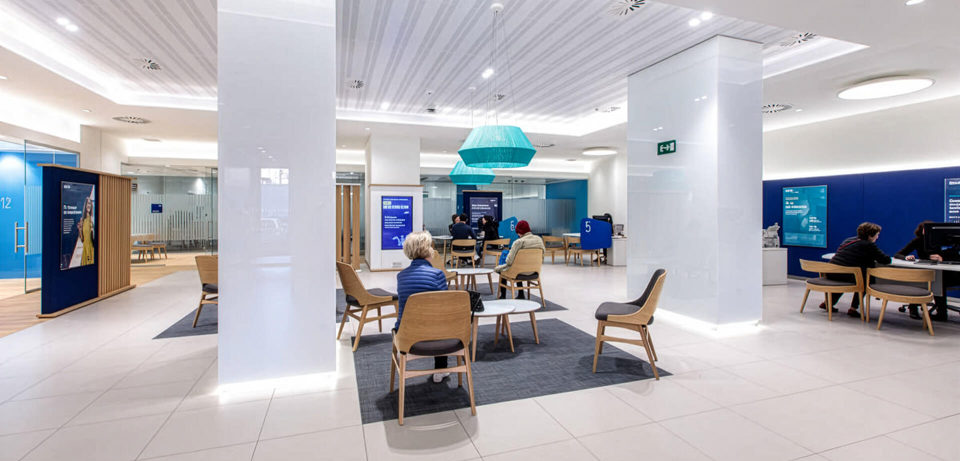 The image displays the interior of a BBVA bank, specifically one of its "Blue Branch" offices. This modern office design focuses on financial advice and a highly digitized customer experience. 