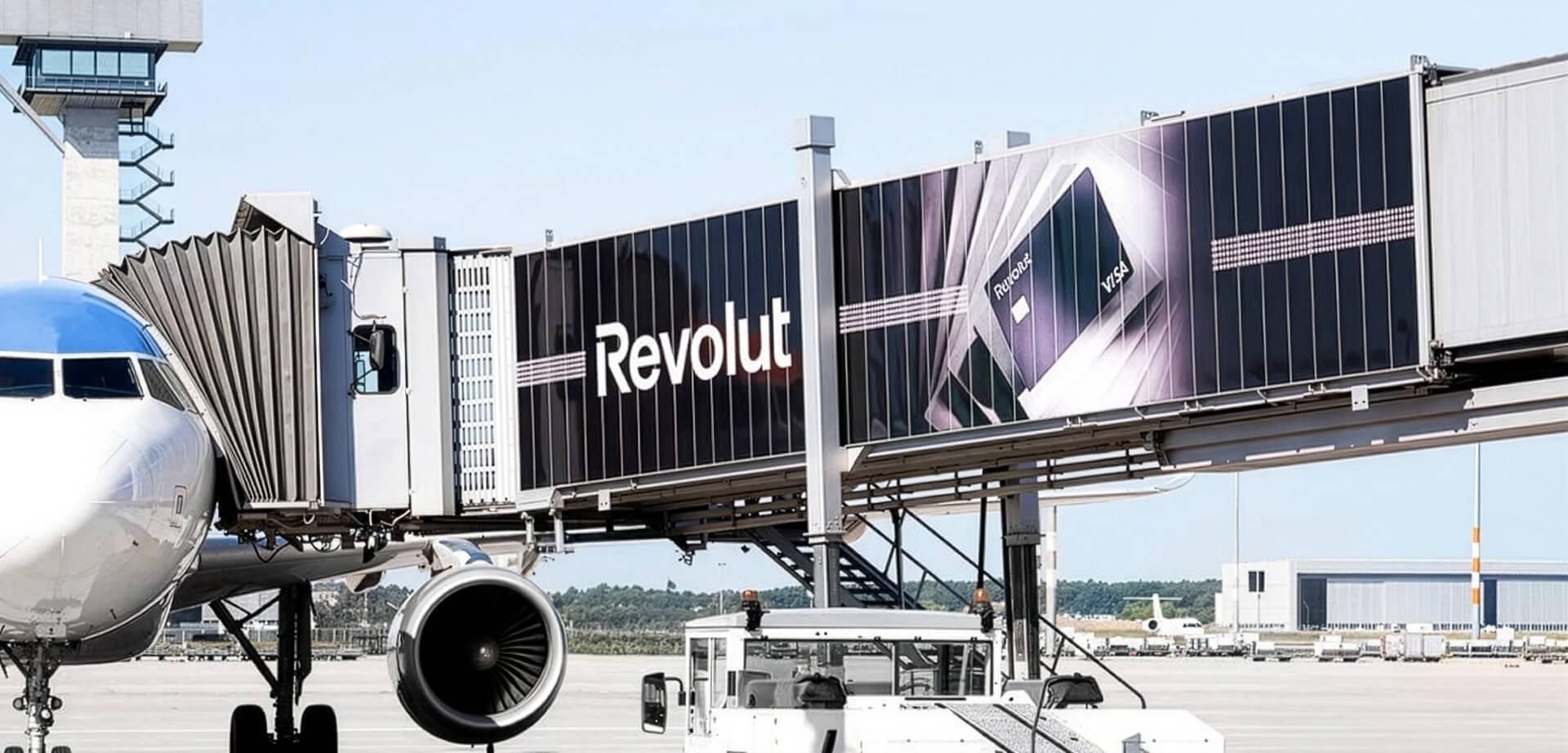 This image shows prominent advertising for the fintech company Revolut placed on a passenger boarding bridge at an airport. Revolut is a digital banking app and payment platform offering travel-related financial services like currency exchange.