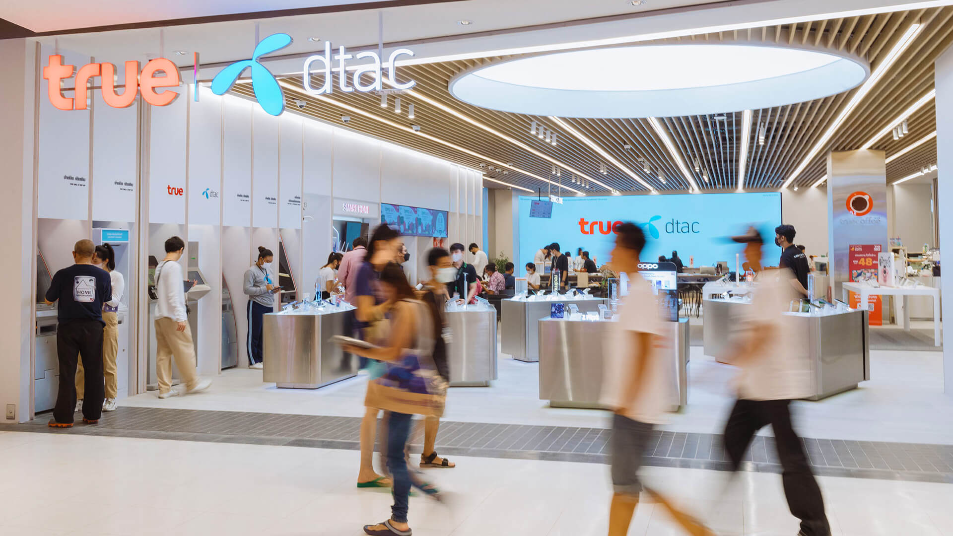 This image shows a modern True Corporation retail store in a shopping mall in Thailand, which serves as a service and sales hub. Following the 2021 merger between True and dtac, these combined locations transitioned to a paperless, AI-driven customer service model.