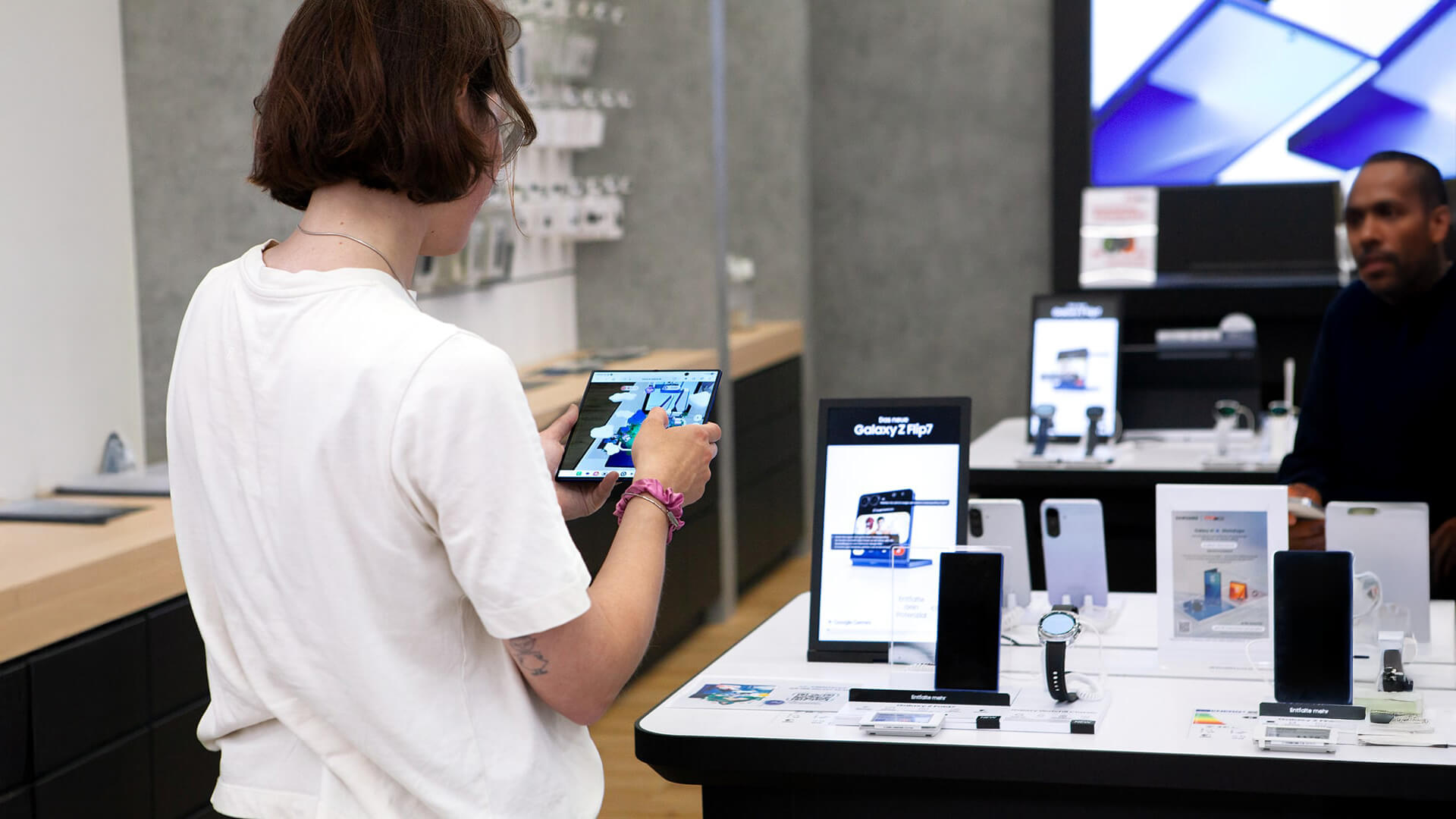 This image shows a customer exploring a foldable smartphone, likely the Samsung Galaxy Z Fold or Galaxy Z Flip, inside a Samsung Experience Store.
