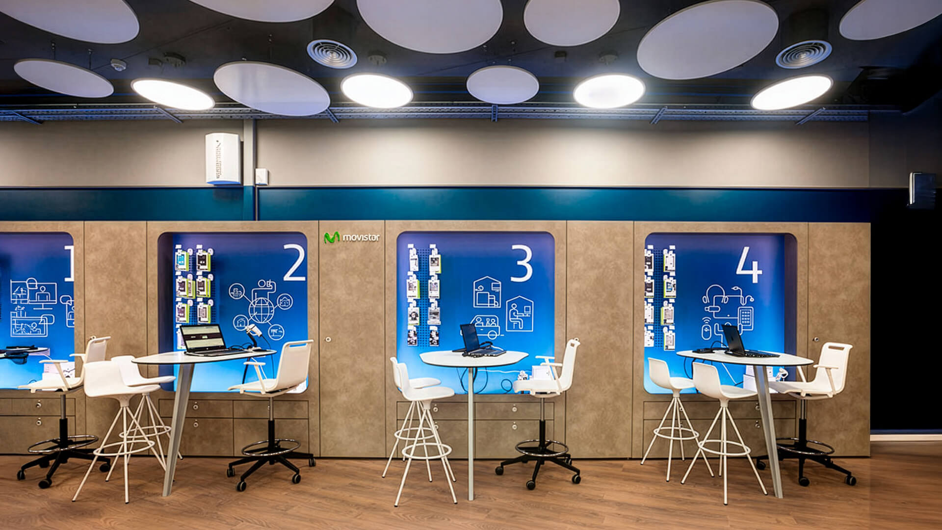 Movistar flagship retail store, designed with semi-private consultation pods featuring high-top seating, integrated laptops, and interactive brand graphics.