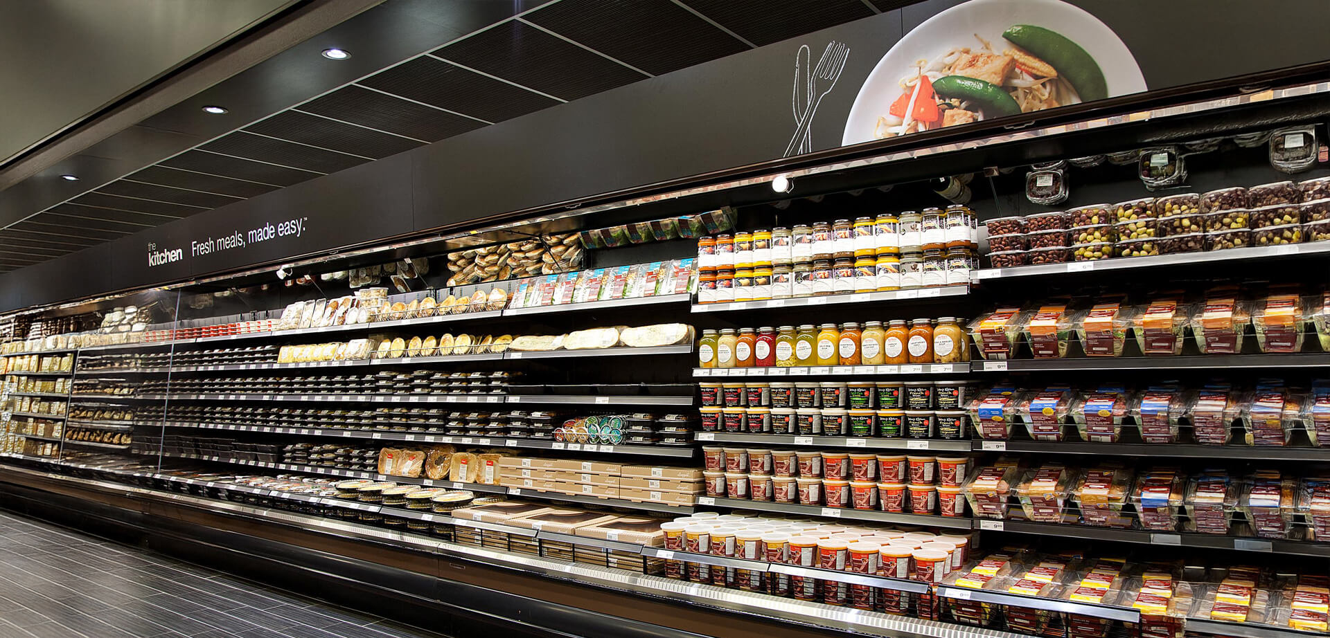 Longo's supermarket, specifically showcasing its prepared meals section branded as "The Kitchen: Fresh meals, made easy". Longo's, a Canadian grocery chain, uses this branding for its in-house line of various prepared foods, including pizzas, sides, and entrées.