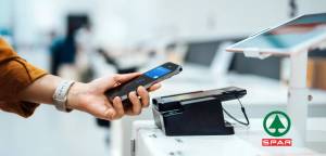 A smartphone makes a contactless payment at a point-of-sale terminal, likely at a SPAR store.